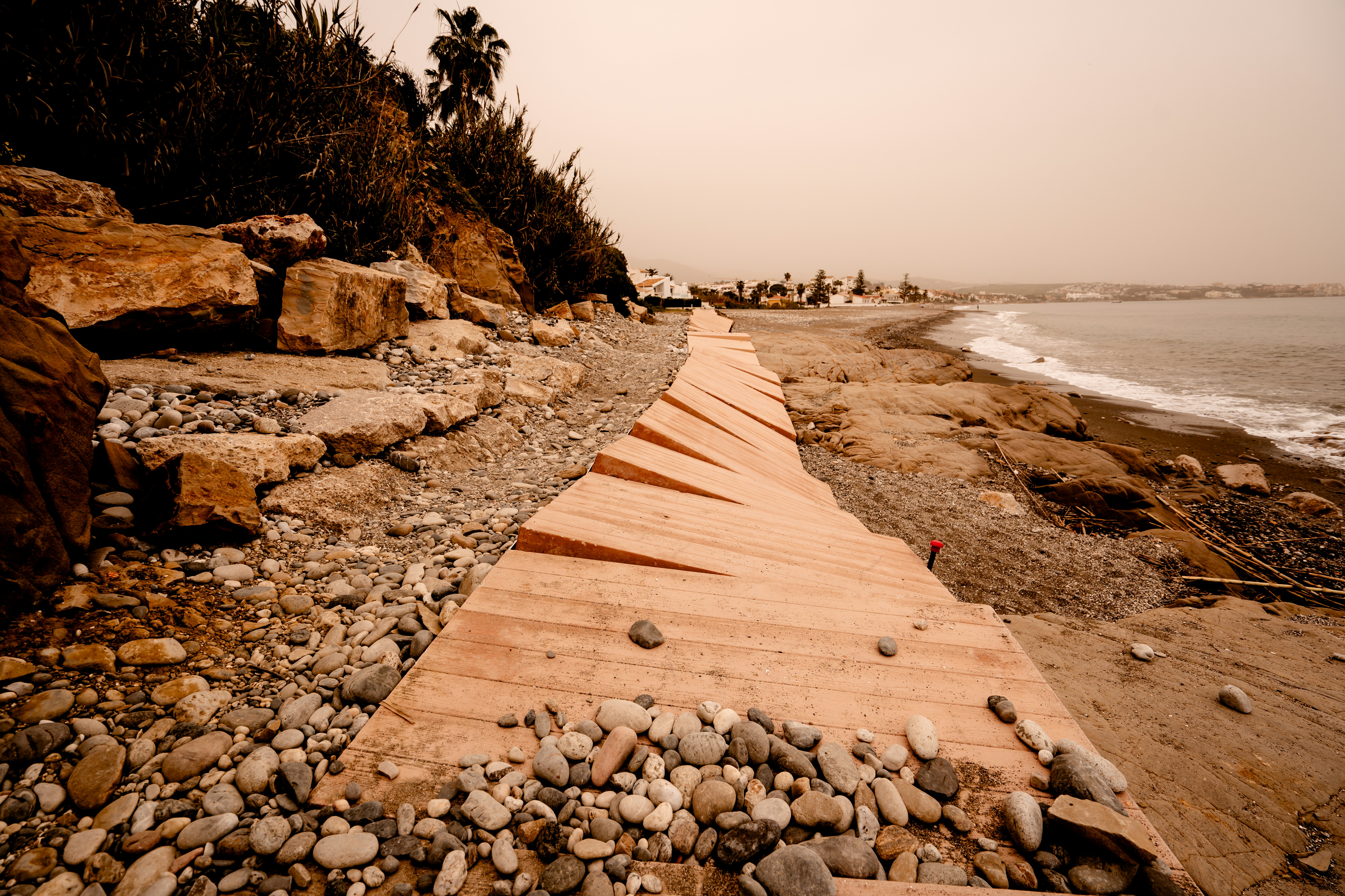 a wooden walkway on a rocky beach next to the ocean, 