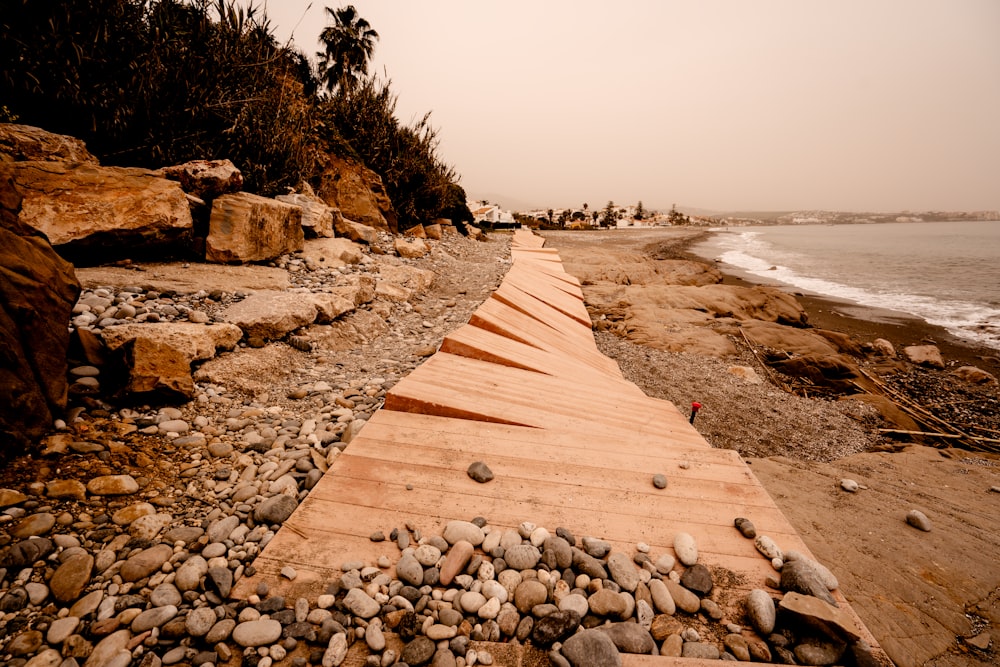 a wooden walkway on a rocky beach next to the ocean