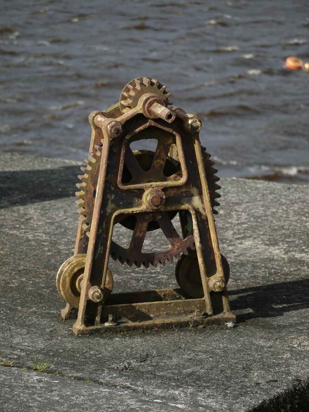 an old clock sitting on top of a rock near the water