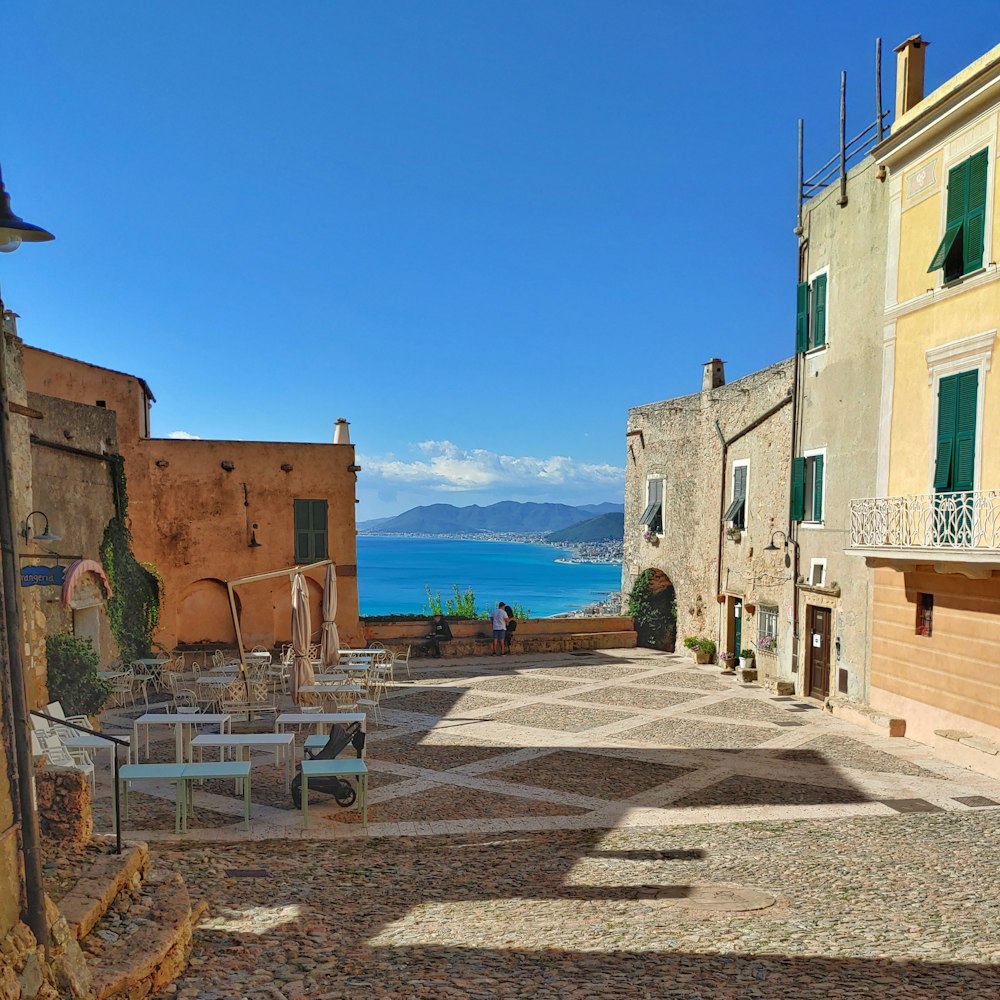 a cobblestone street lined with tables and chairs next to a body of water