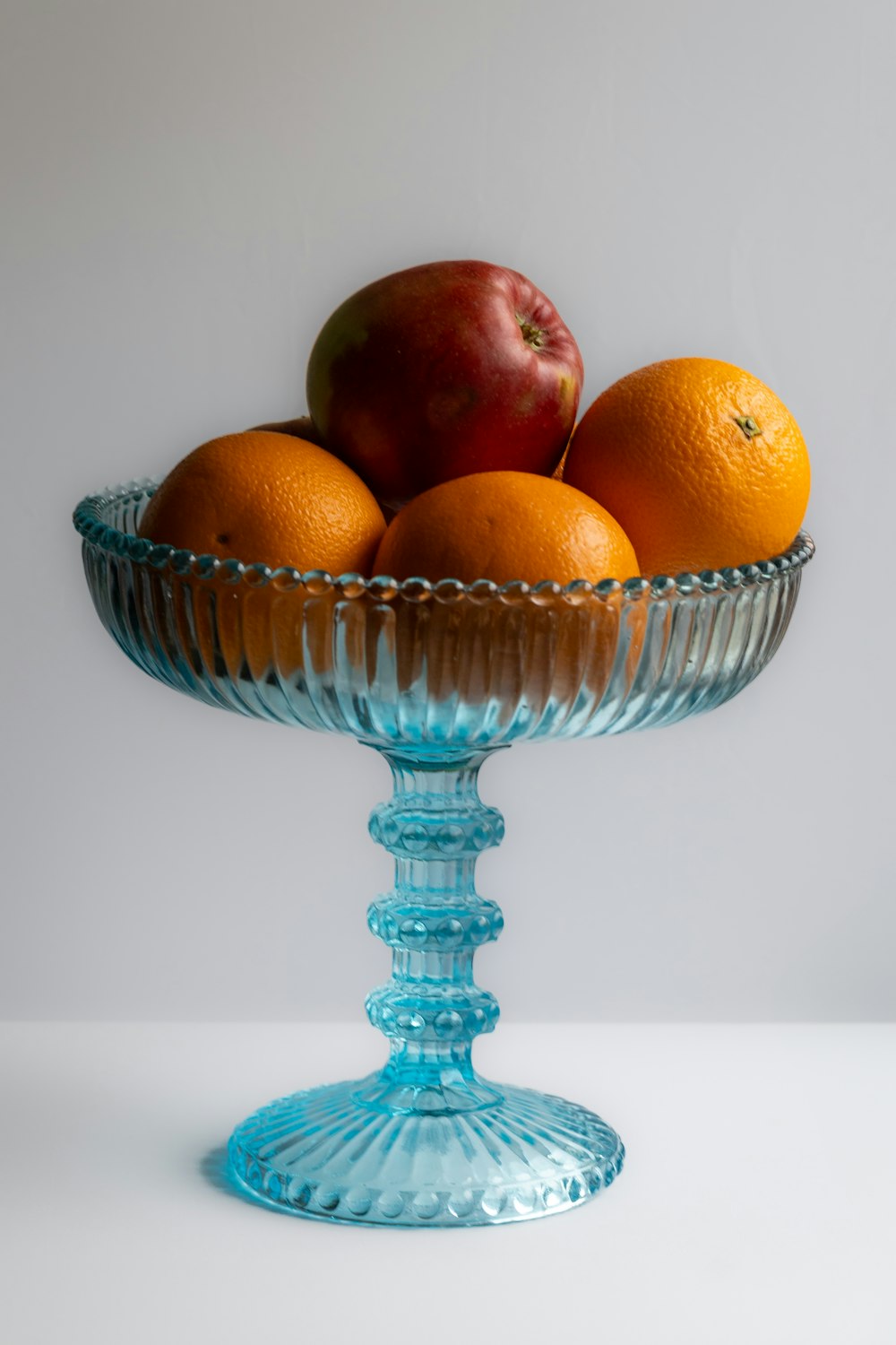 a glass bowl filled with oranges and apples
