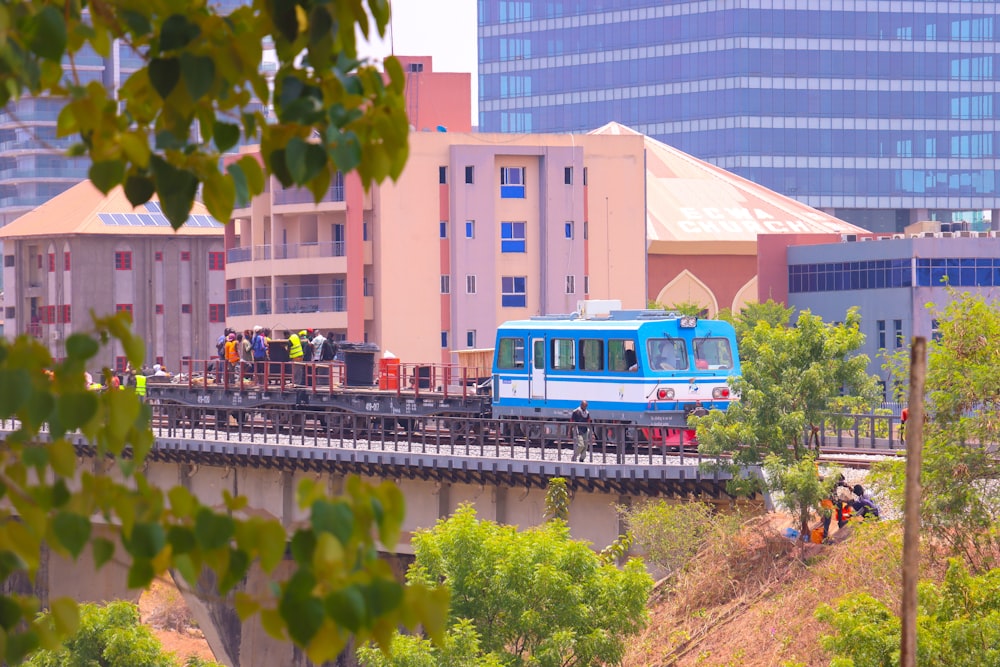 a blue train traveling over a bridge next to tall buildings