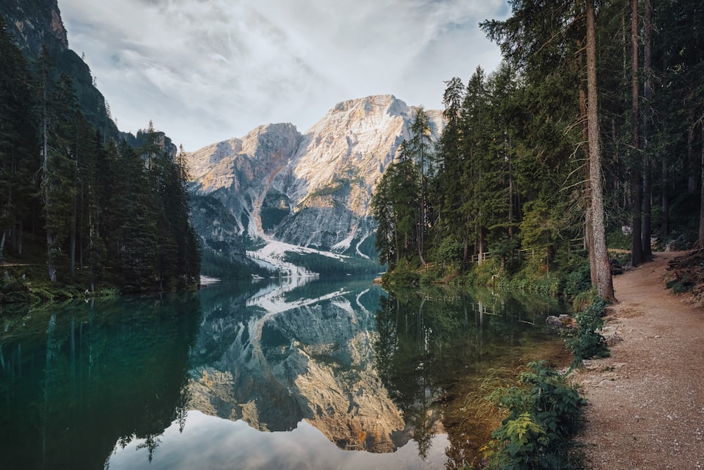 a lake surrounded by trees and mountains under a cloudy sky