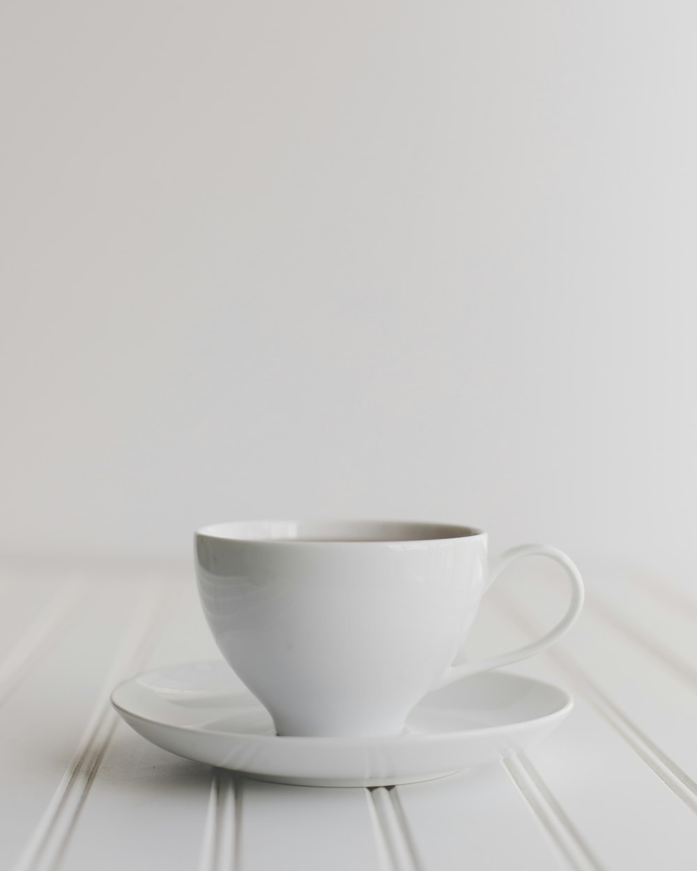 a white cup and saucer on a white table