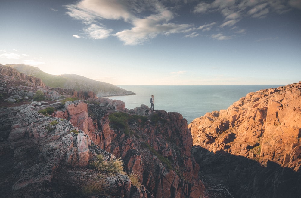 a person standing on top of a mountain next to the ocean