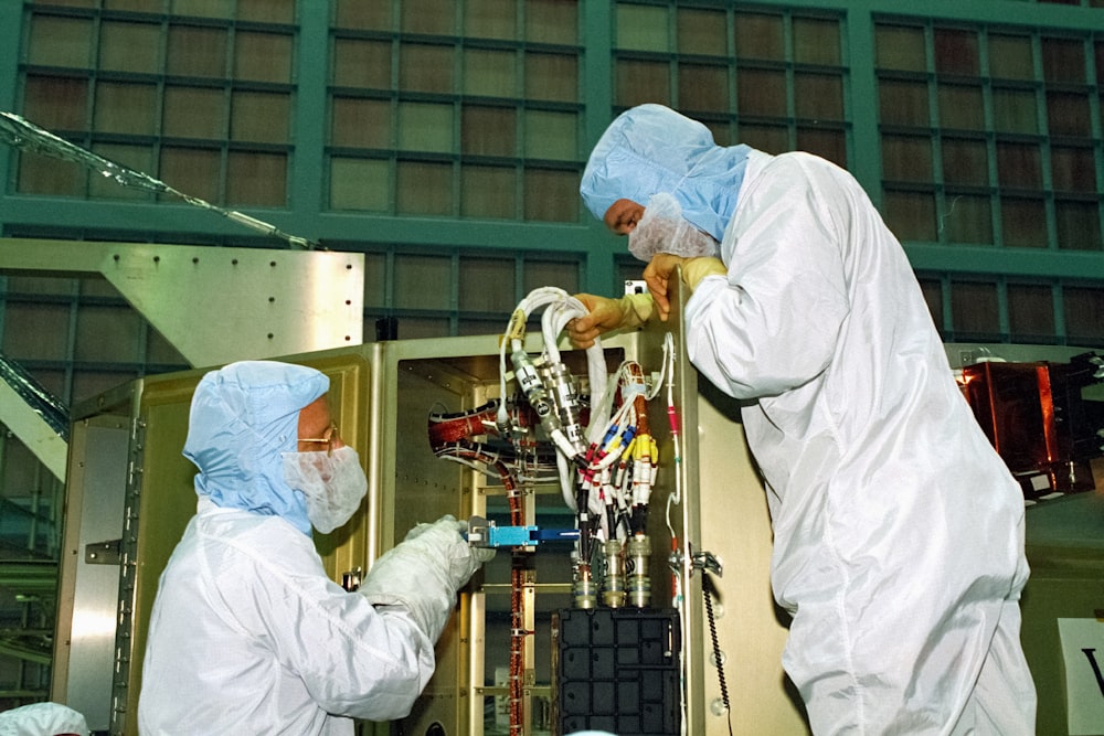 a couple of people in white suits working on a machine