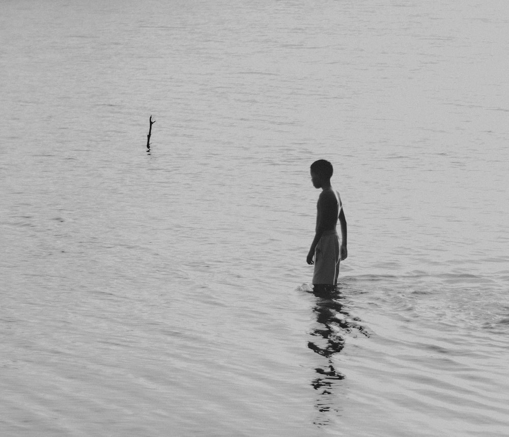 a boy standing in the water looking at a bird