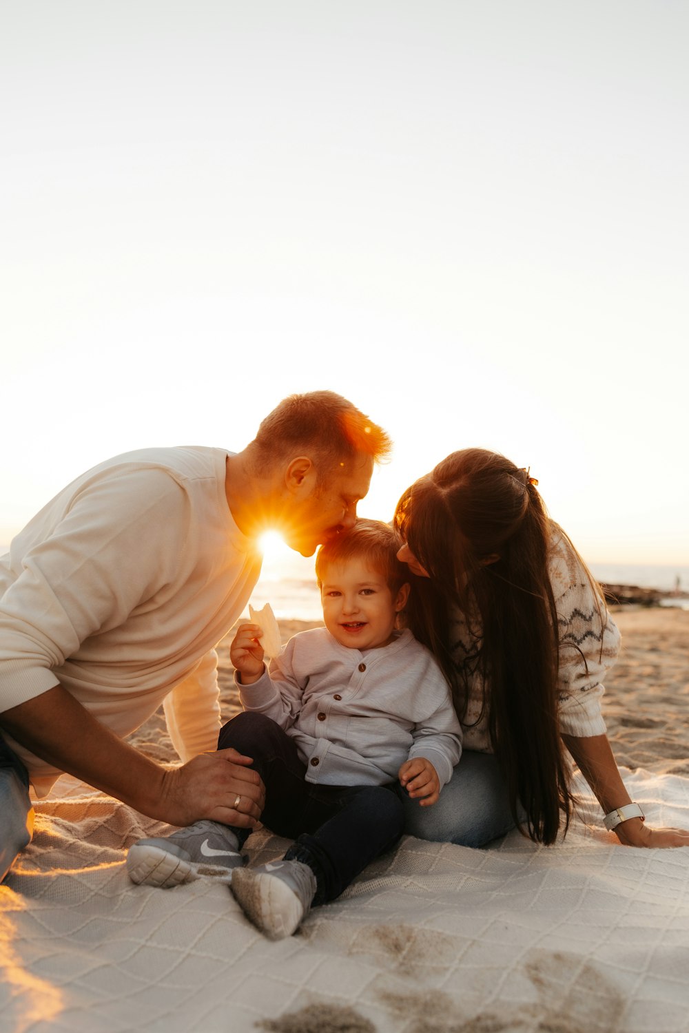 a man, woman and baby on the beach at sunset