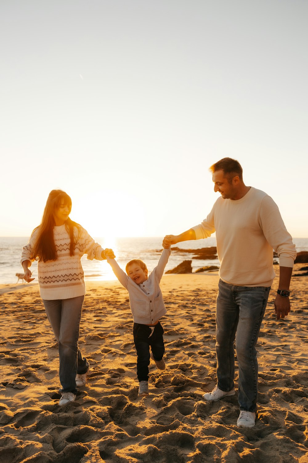 a man and woman holding hands with a child on a beach