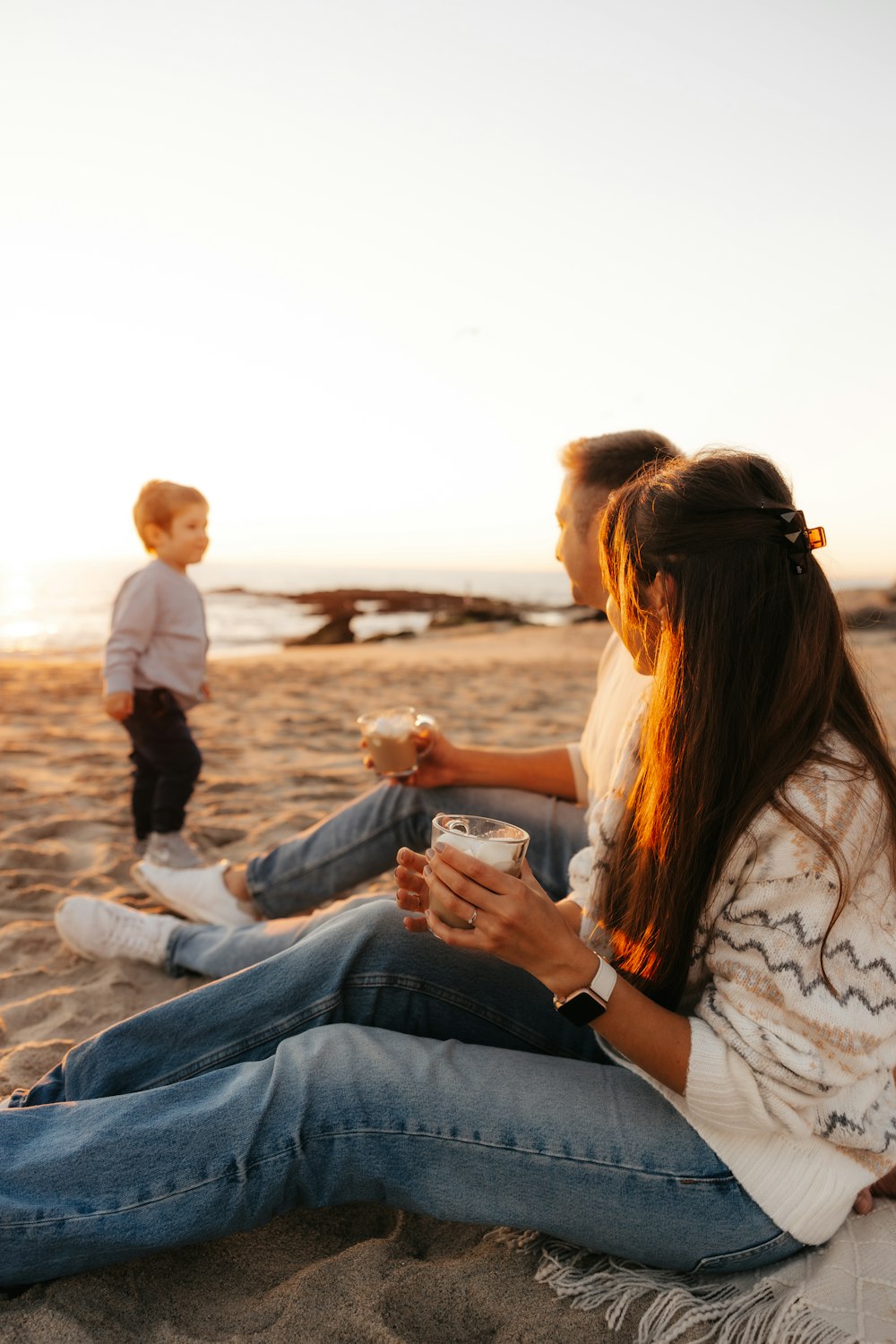 a couple of people sitting on top of a sandy beach