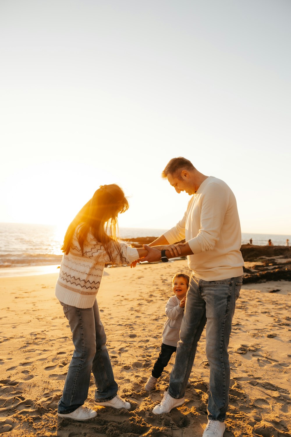 a man and woman holding hands with a child on the beach