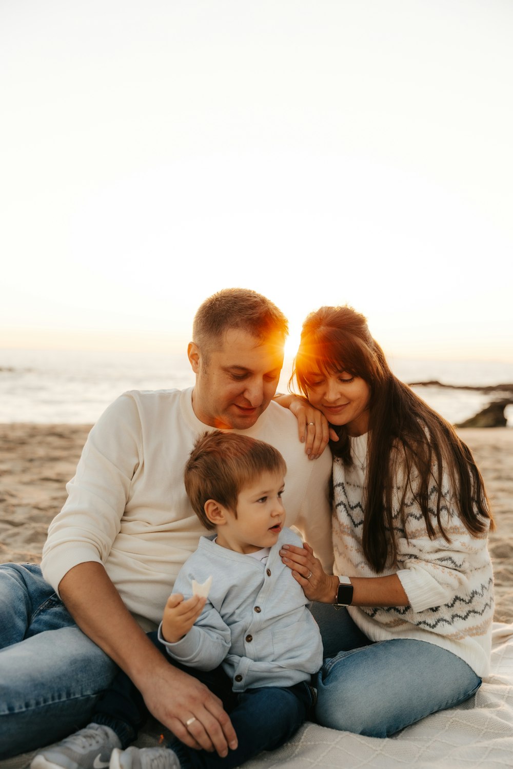 a man and woman sitting on the beach with a baby