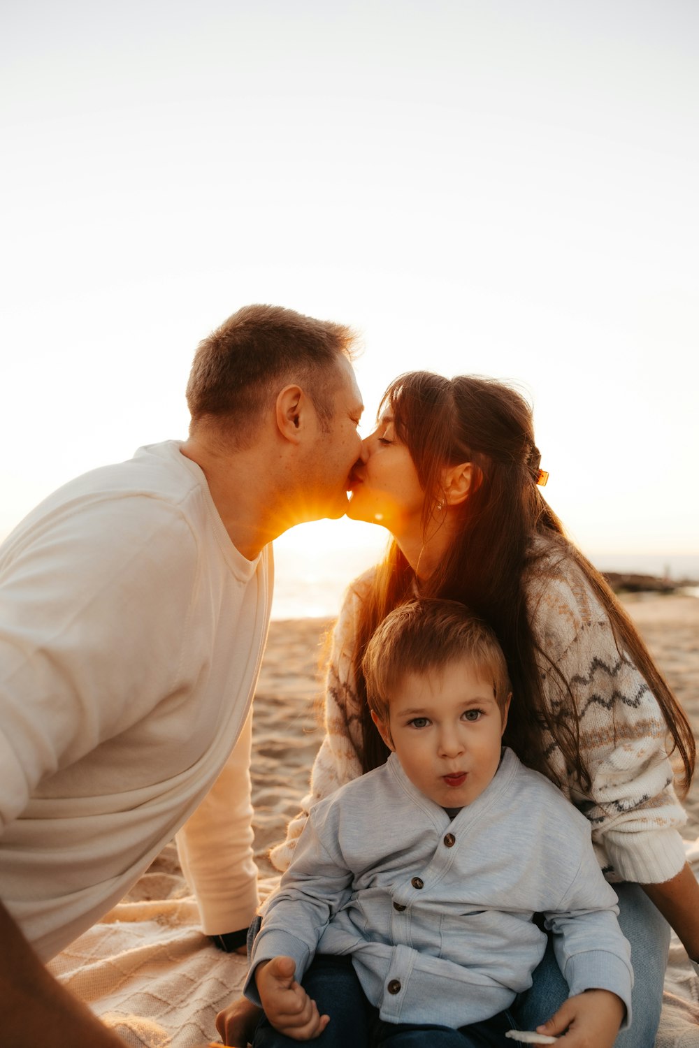 a man and woman kissing a little boy on the beach