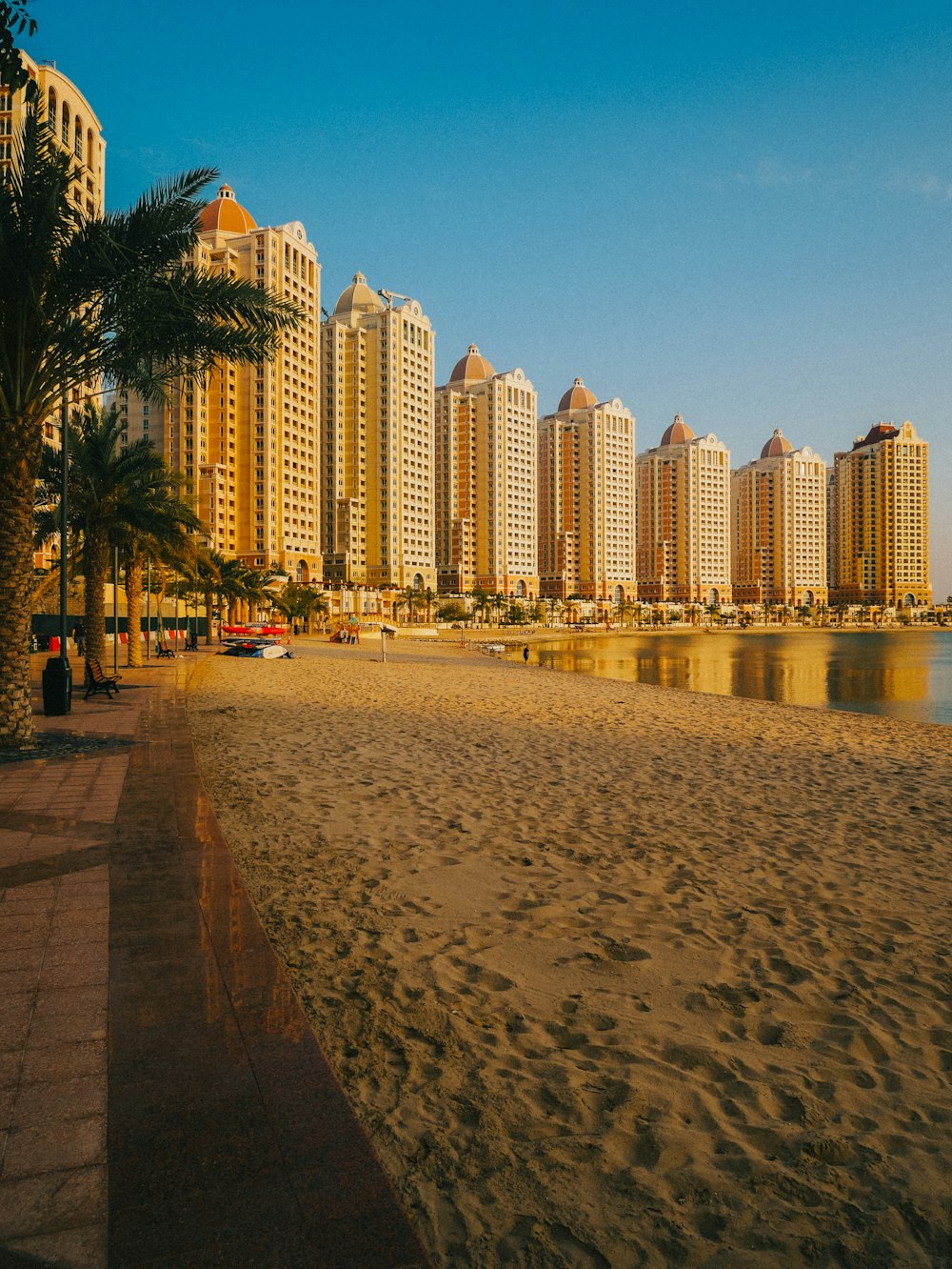 a sandy beach next to tall buildings and palm trees