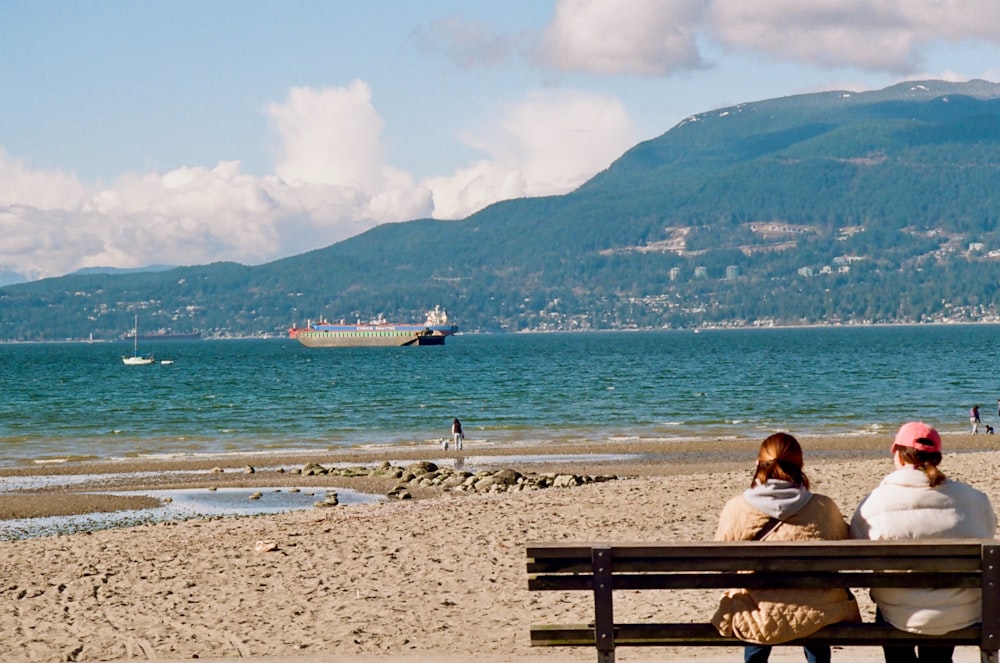 two people sitting on a bench on a beach