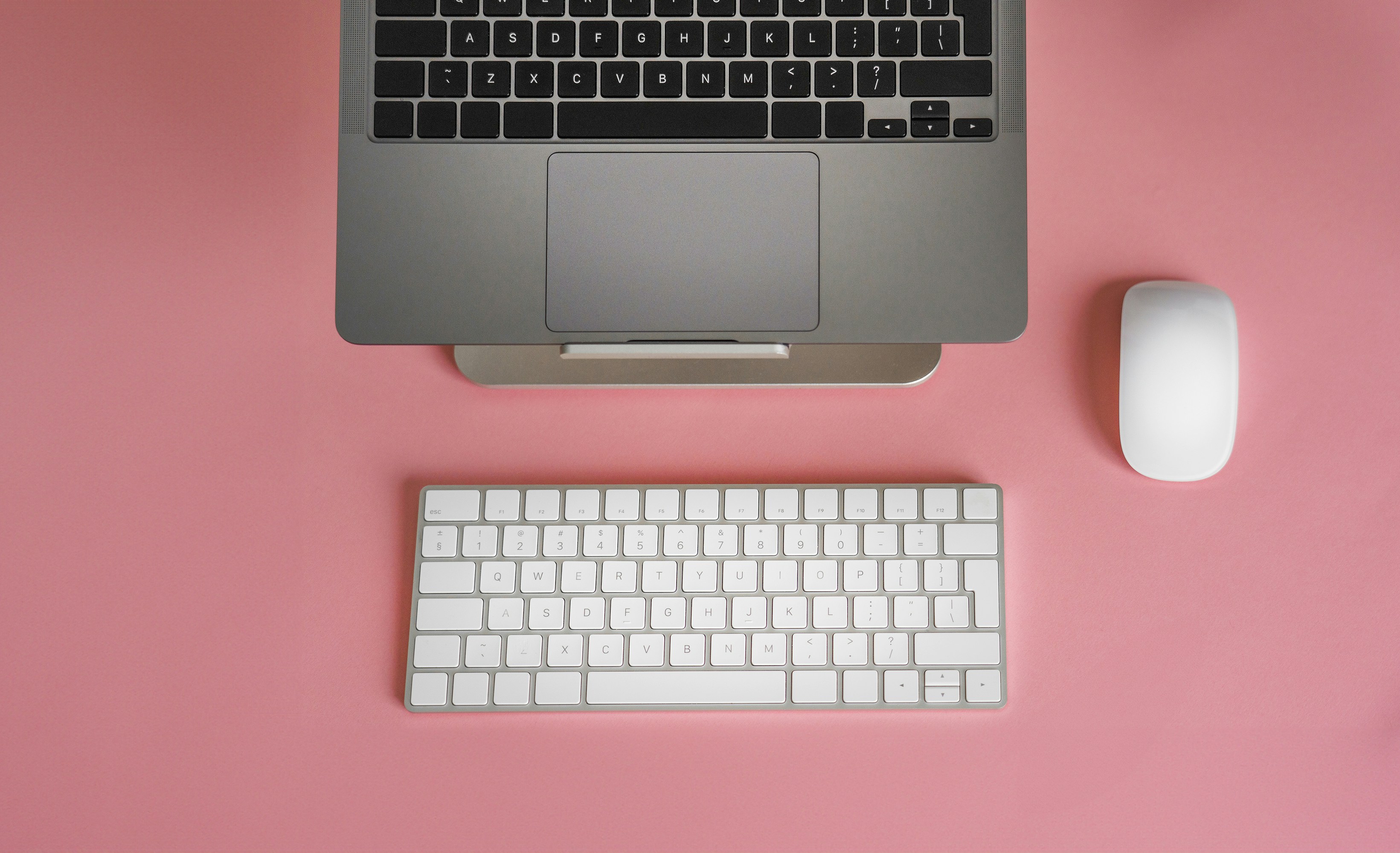 a keyboard, mouse, and laptop on a pink surface