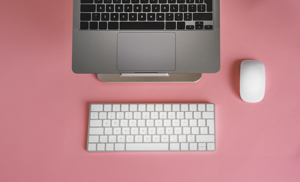 a keyboard, mouse, and laptop on a pink surface