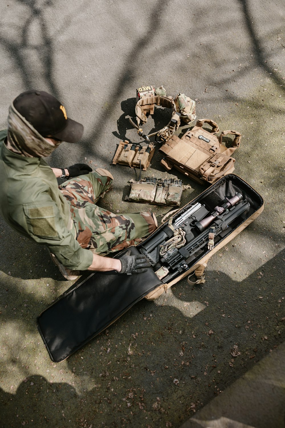 a man sitting on the ground next to a rifle case