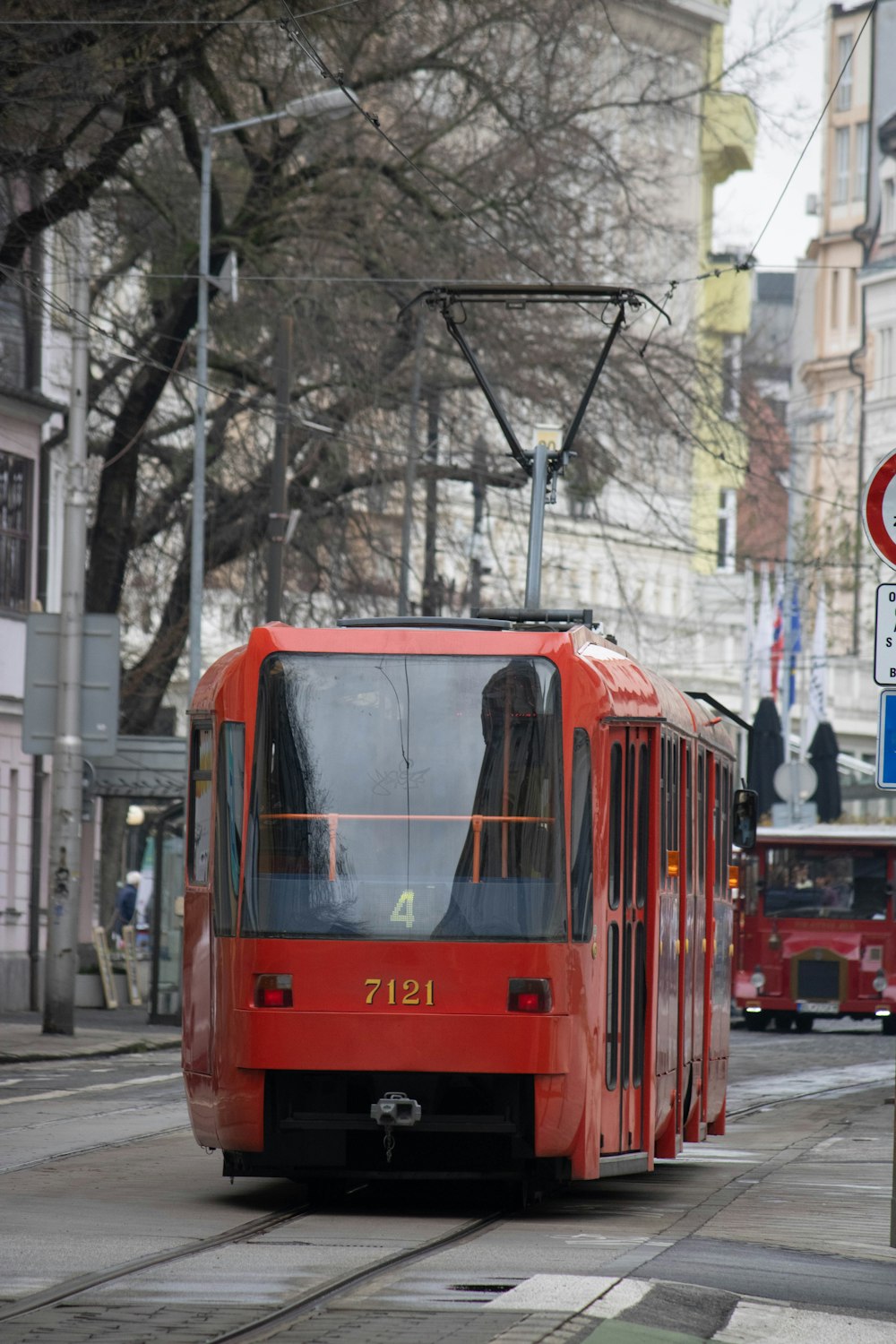 a red trolley car traveling down a street next to tall buildings