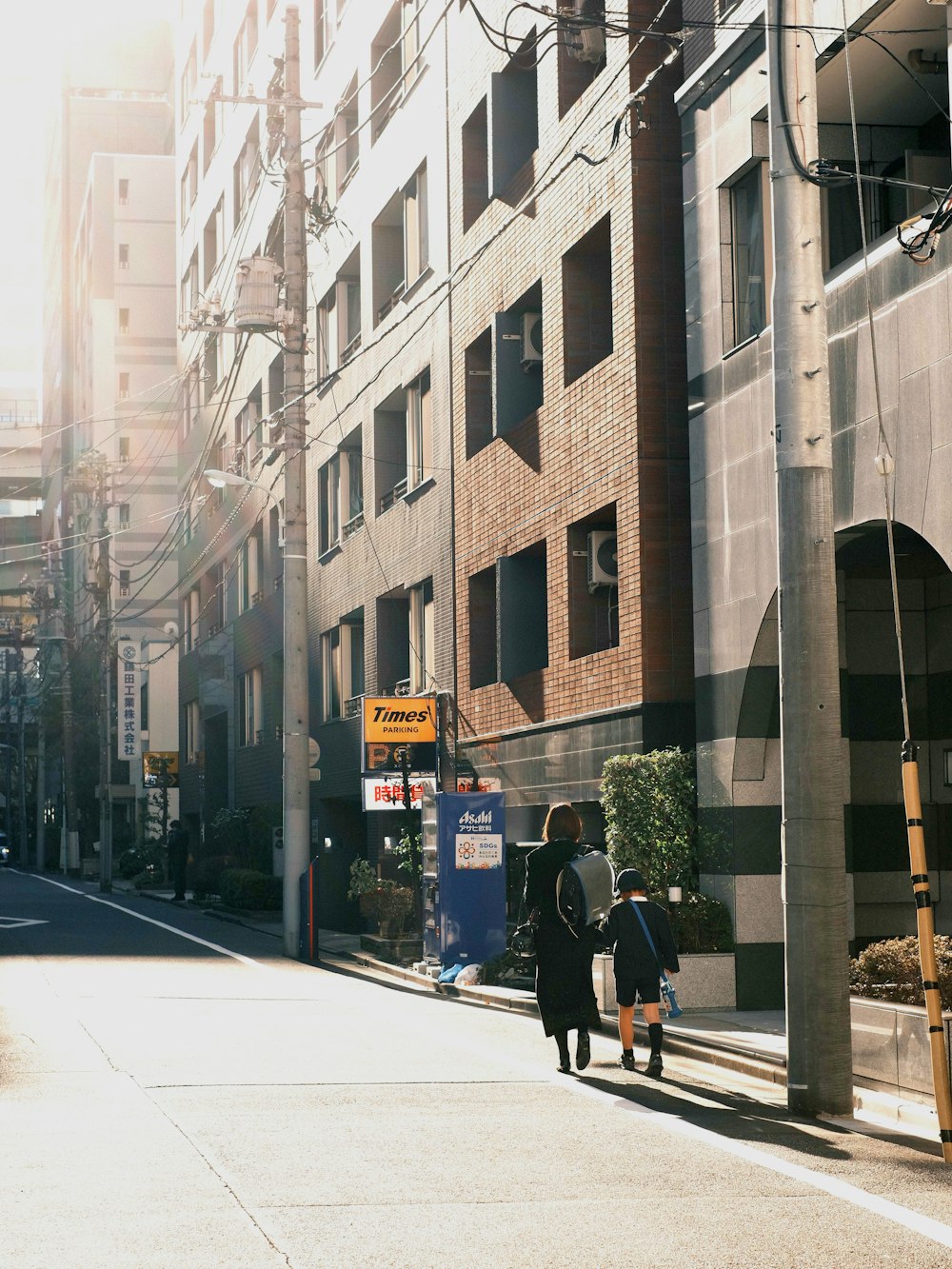 a couple of people walking down a street next to tall buildings