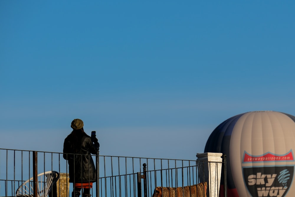 um homem em cima de uma cerca de metal ao lado de um balão de ar quente