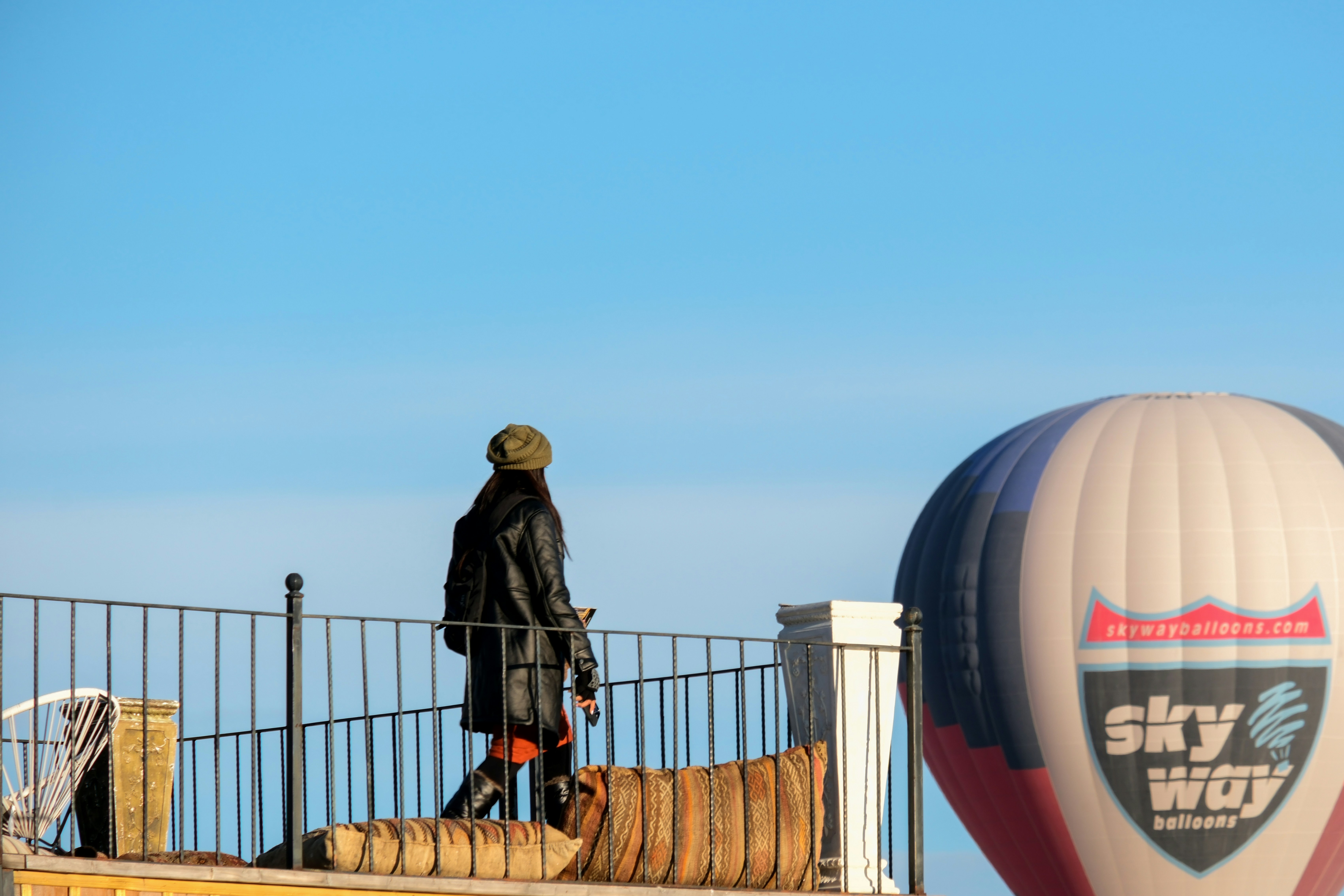 a person standing on a bridge with a hot air balloon in the background - a-person-standing-on-a-bridge-with-a-hot-air-balloon-in-the-background-VUlcIVOX3F0