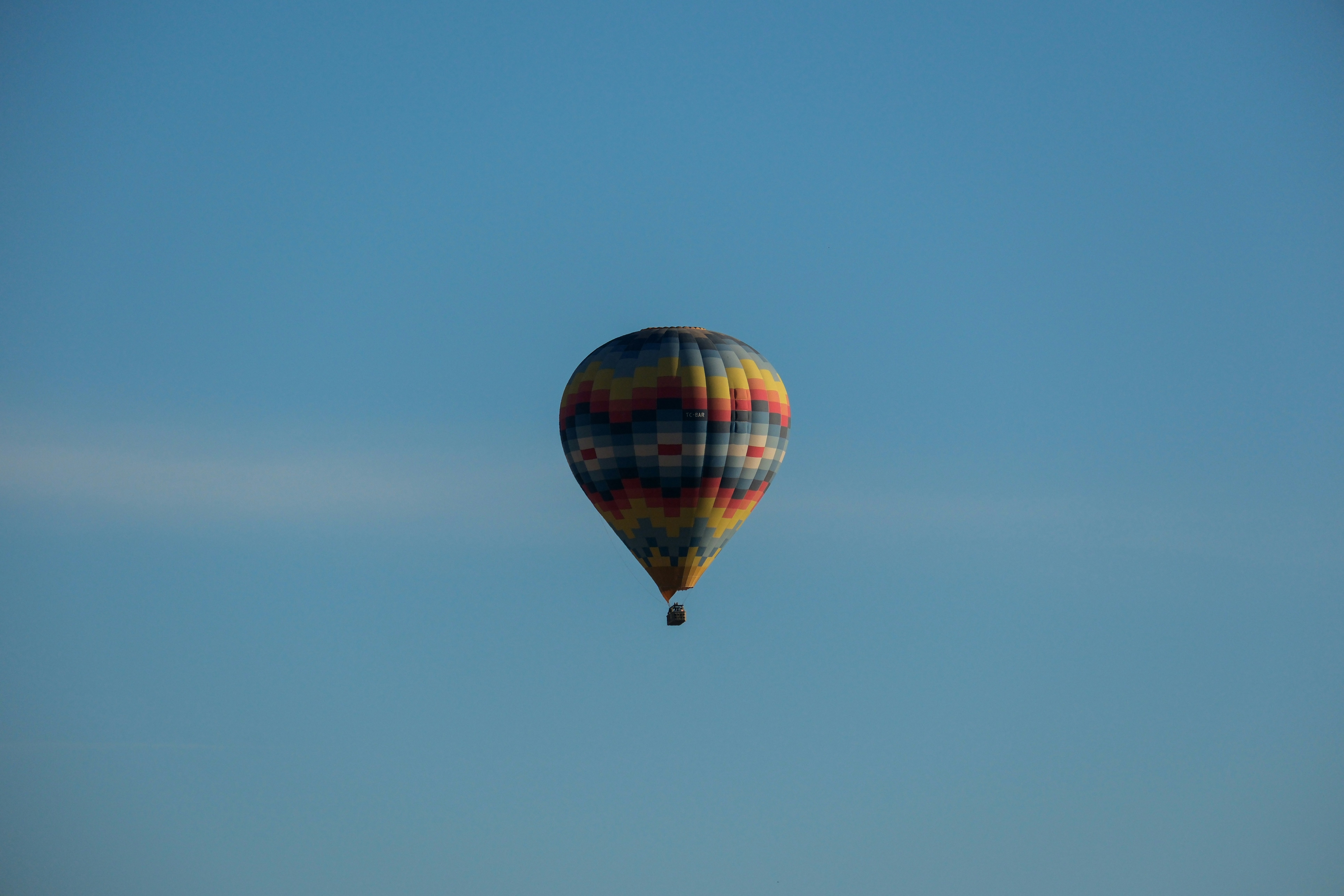 a colorful hot air balloon flying through a blue sky - a-colorful-hot-air-balloon-flying-through-a-blue-sky-MgnLXkbiJIs