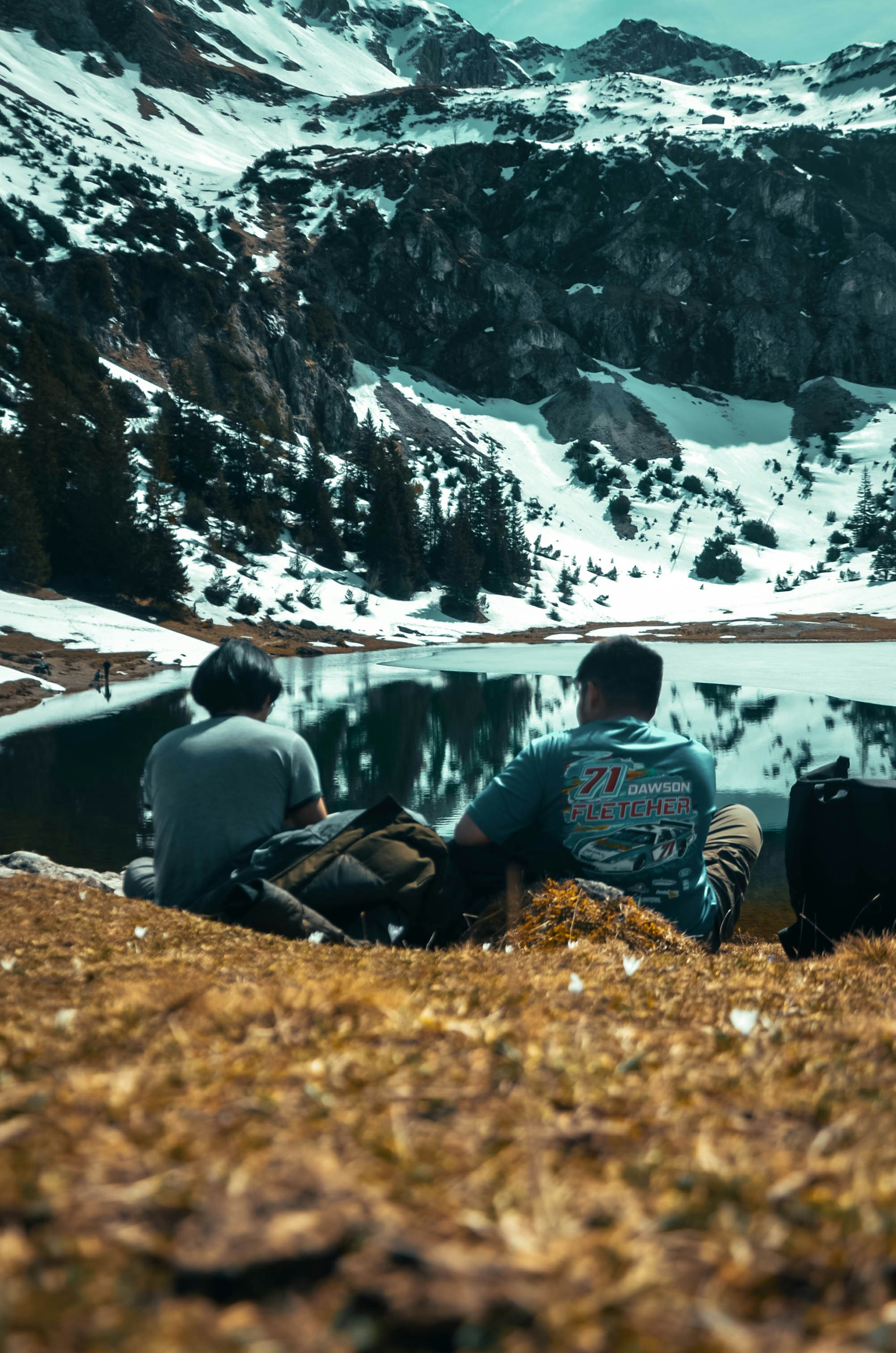 two people sitting on a hill overlooking a lake