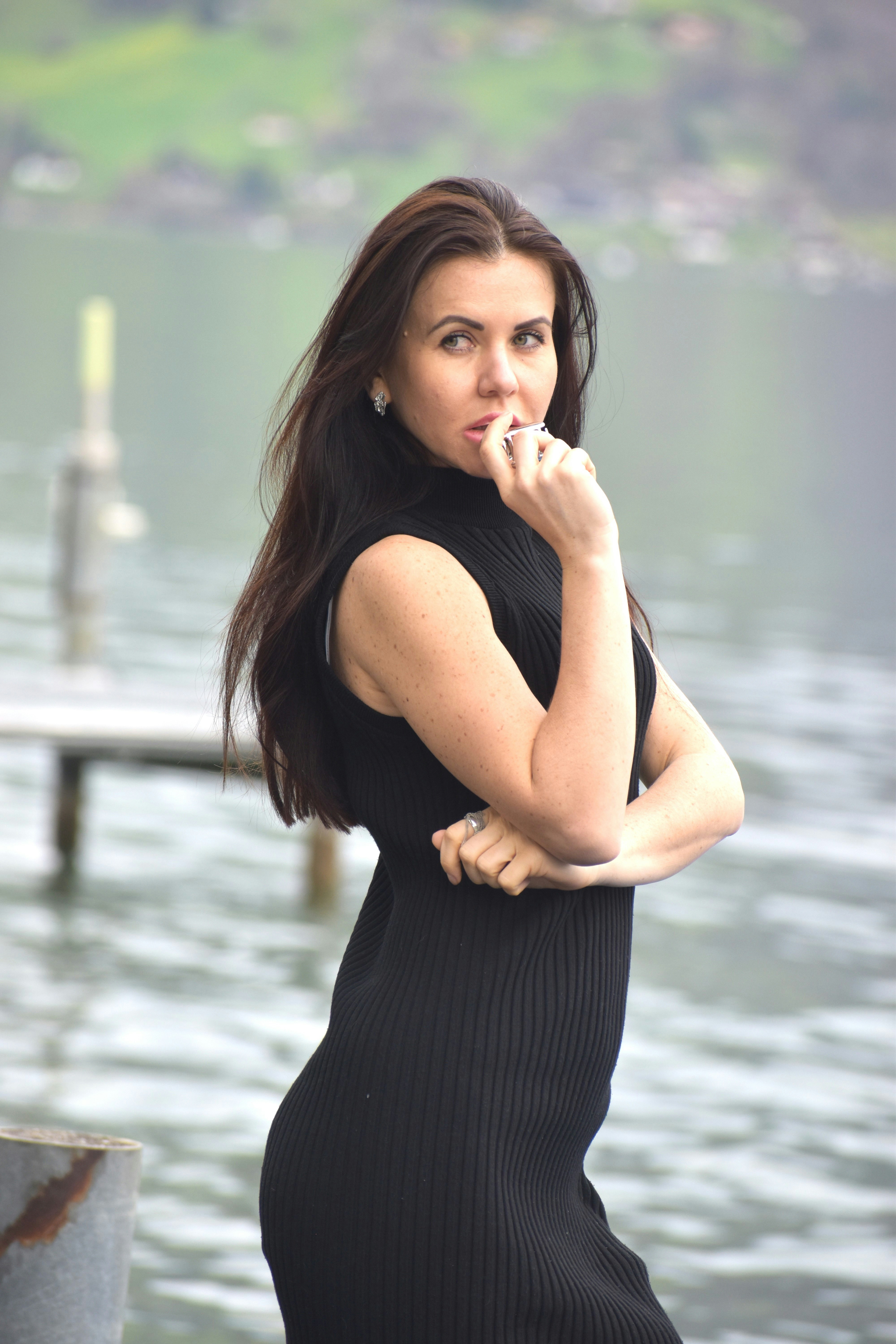 a woman in a black dress standing by a body of water