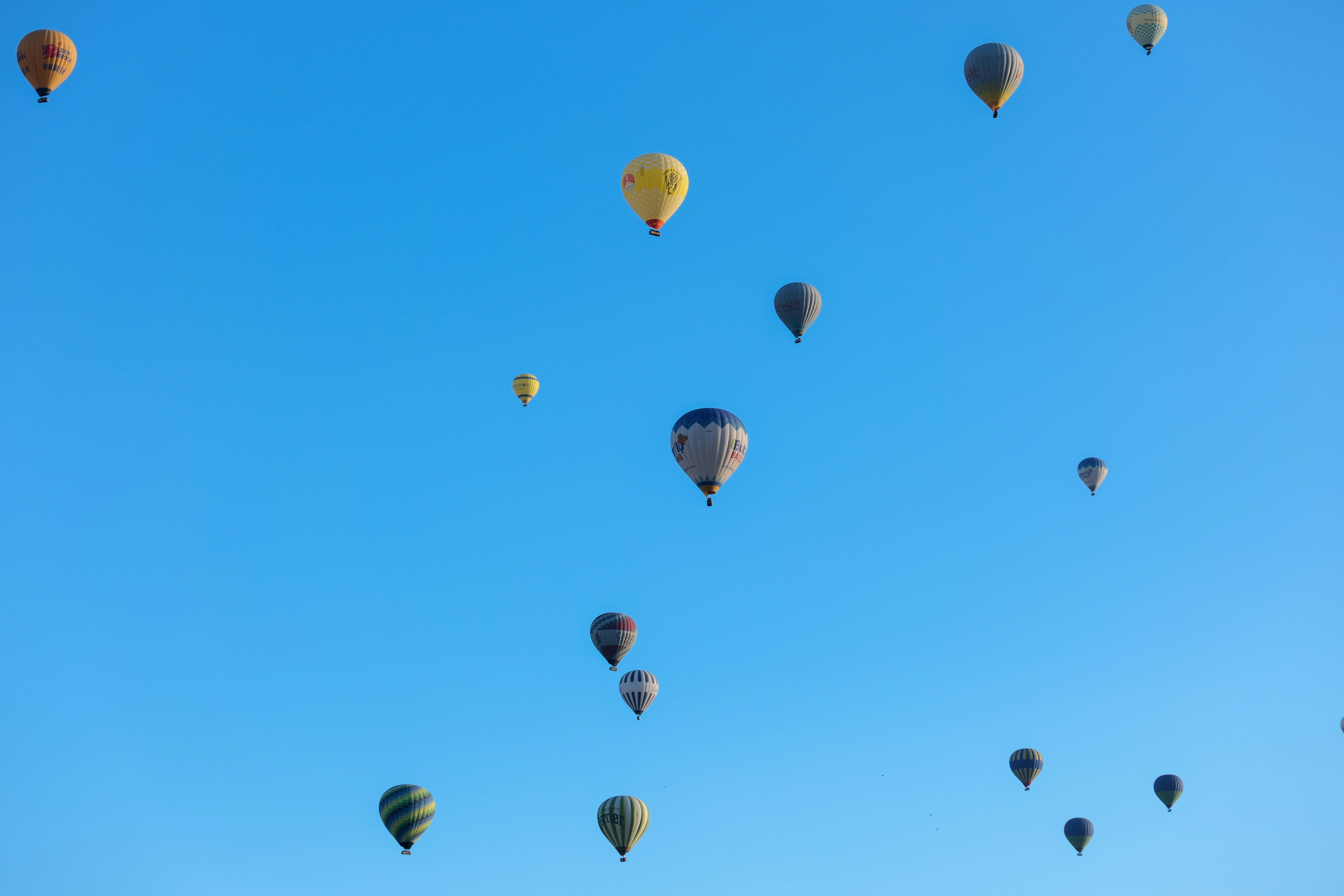 a group of hot air balloons flying through a blue sky - a-group-of-hot-air-balloons-flying-through-a-blue-sky-XvJL06bNAv0