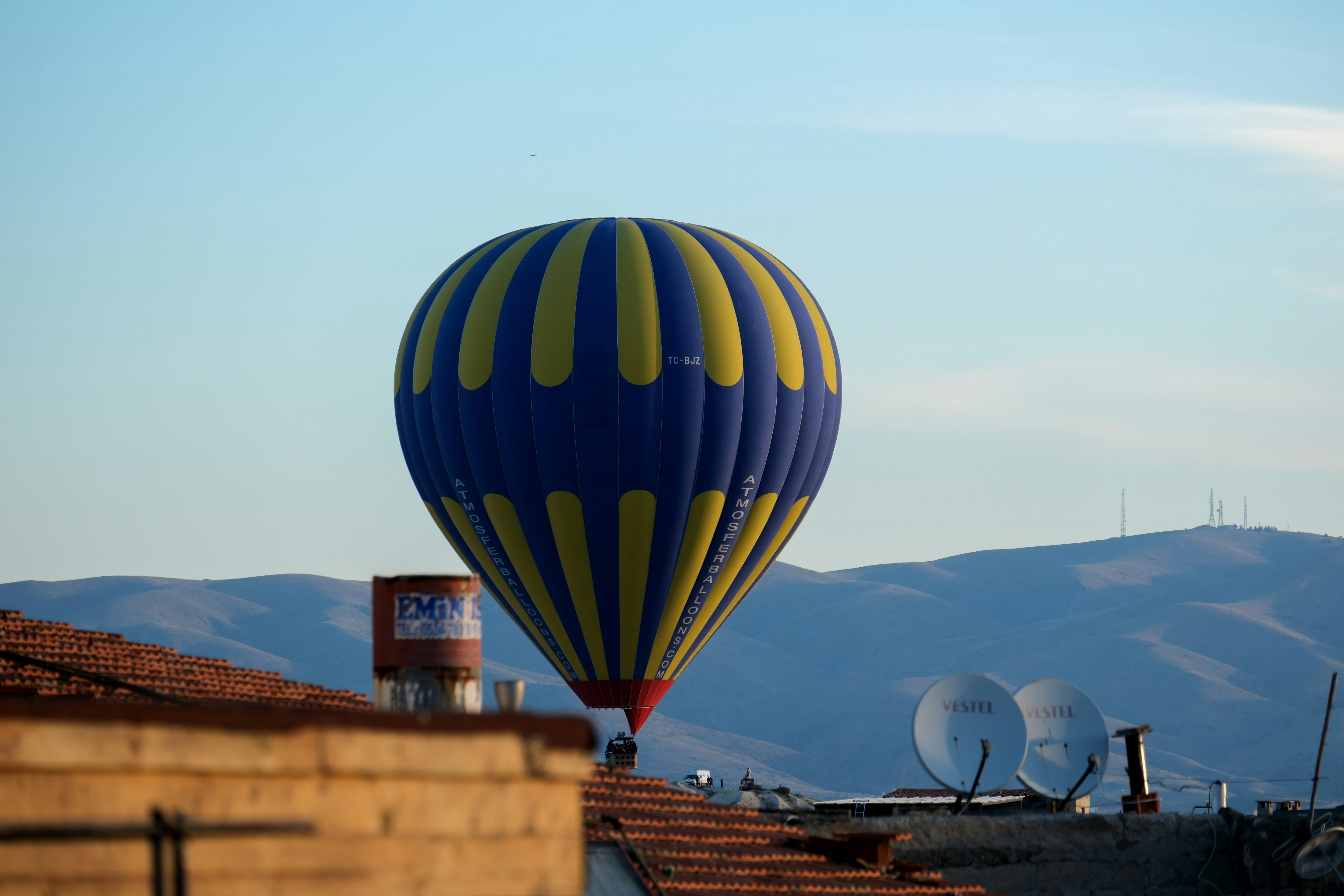 a blue and yellow hot air balloon flying over rooftops - a-blue-and-yellow-hot-air-balloon-flying-over-rooftops-lxglHxJ4qKo