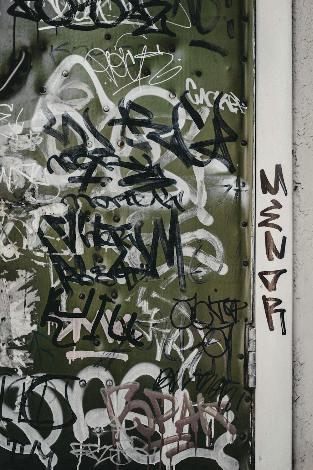 a door covered in lots of graffiti next to a wall