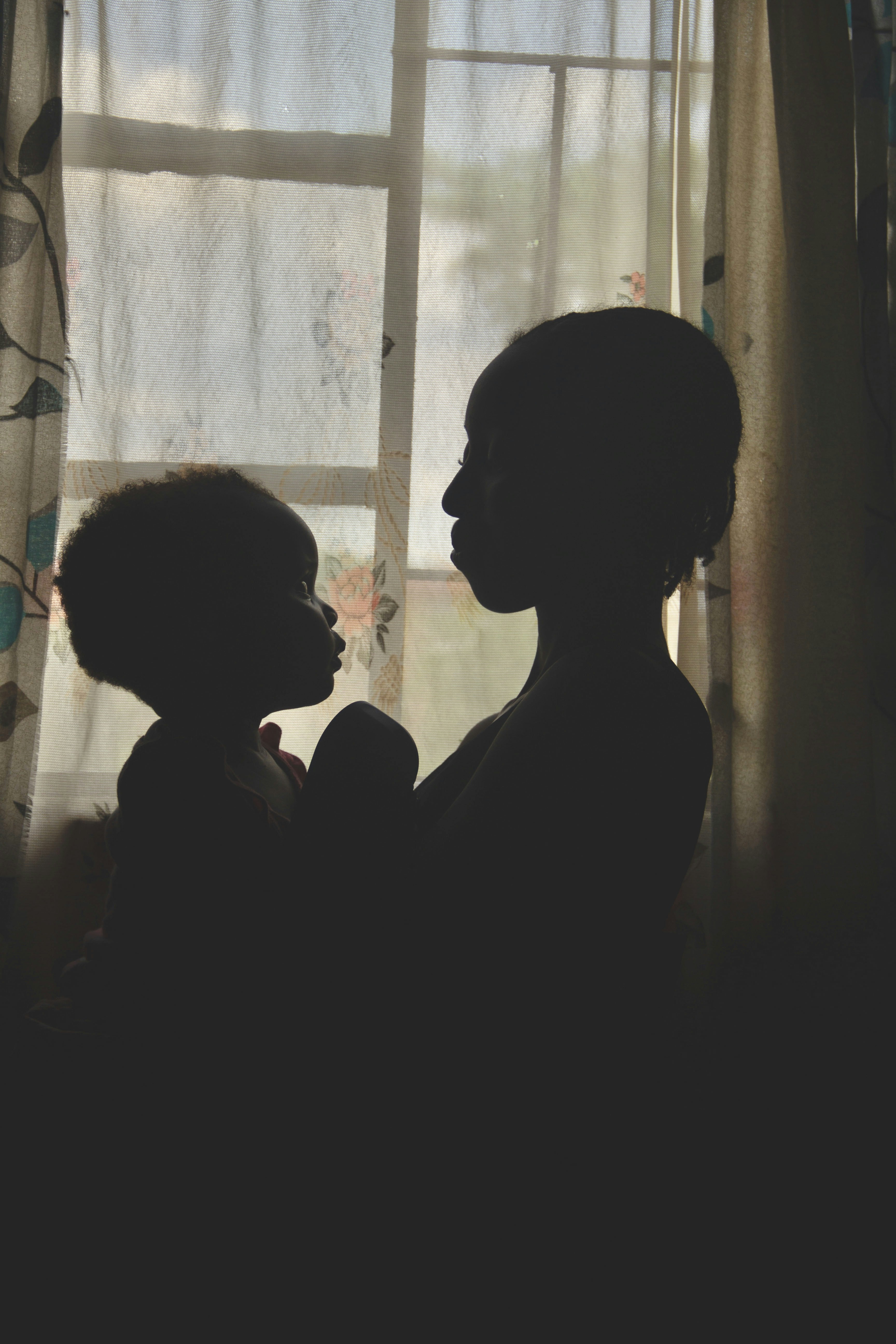 siluet seorang wanita menggendong bayi di depan jendela