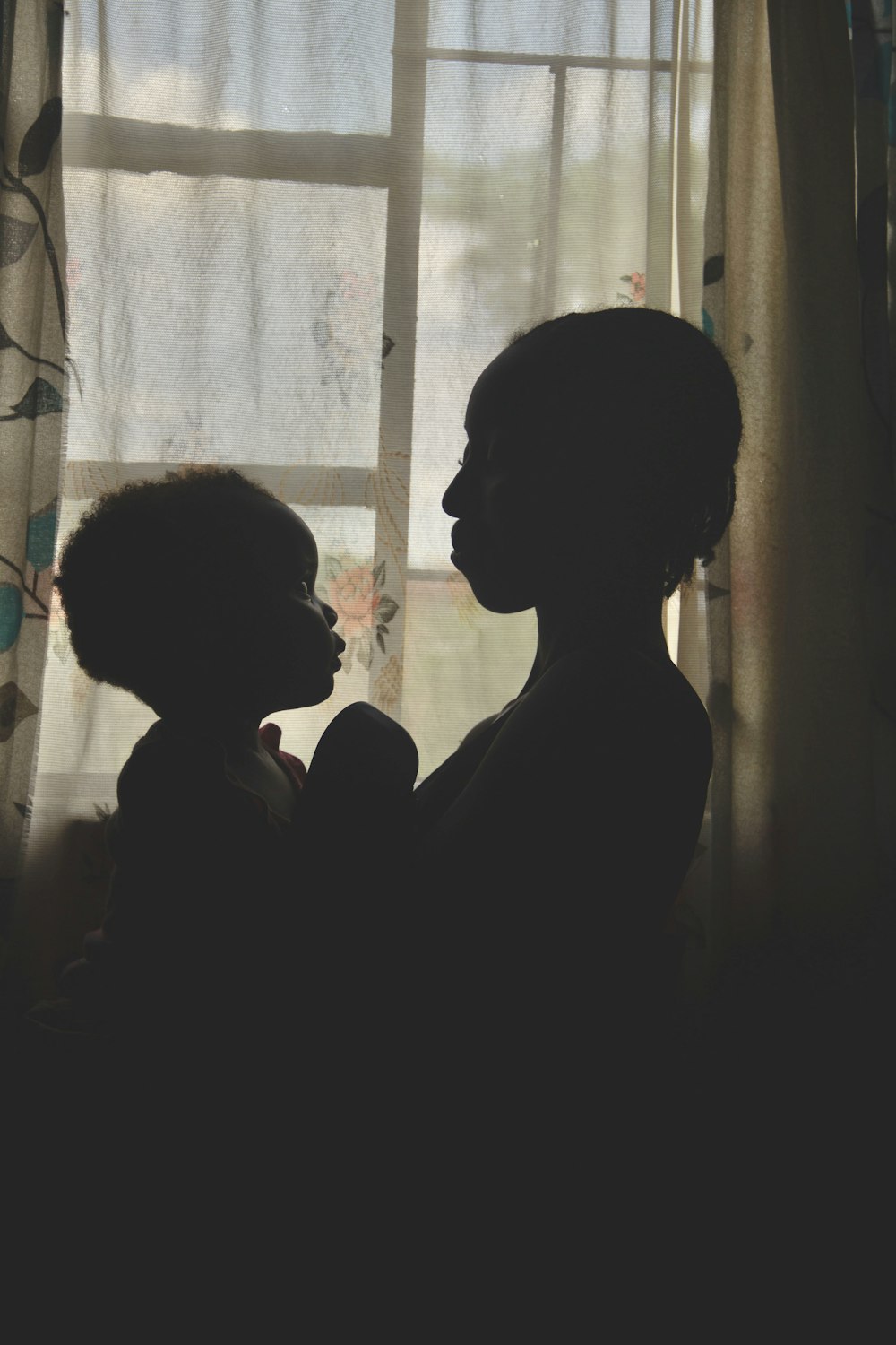 a silhouette of a woman holding a baby in front of a window