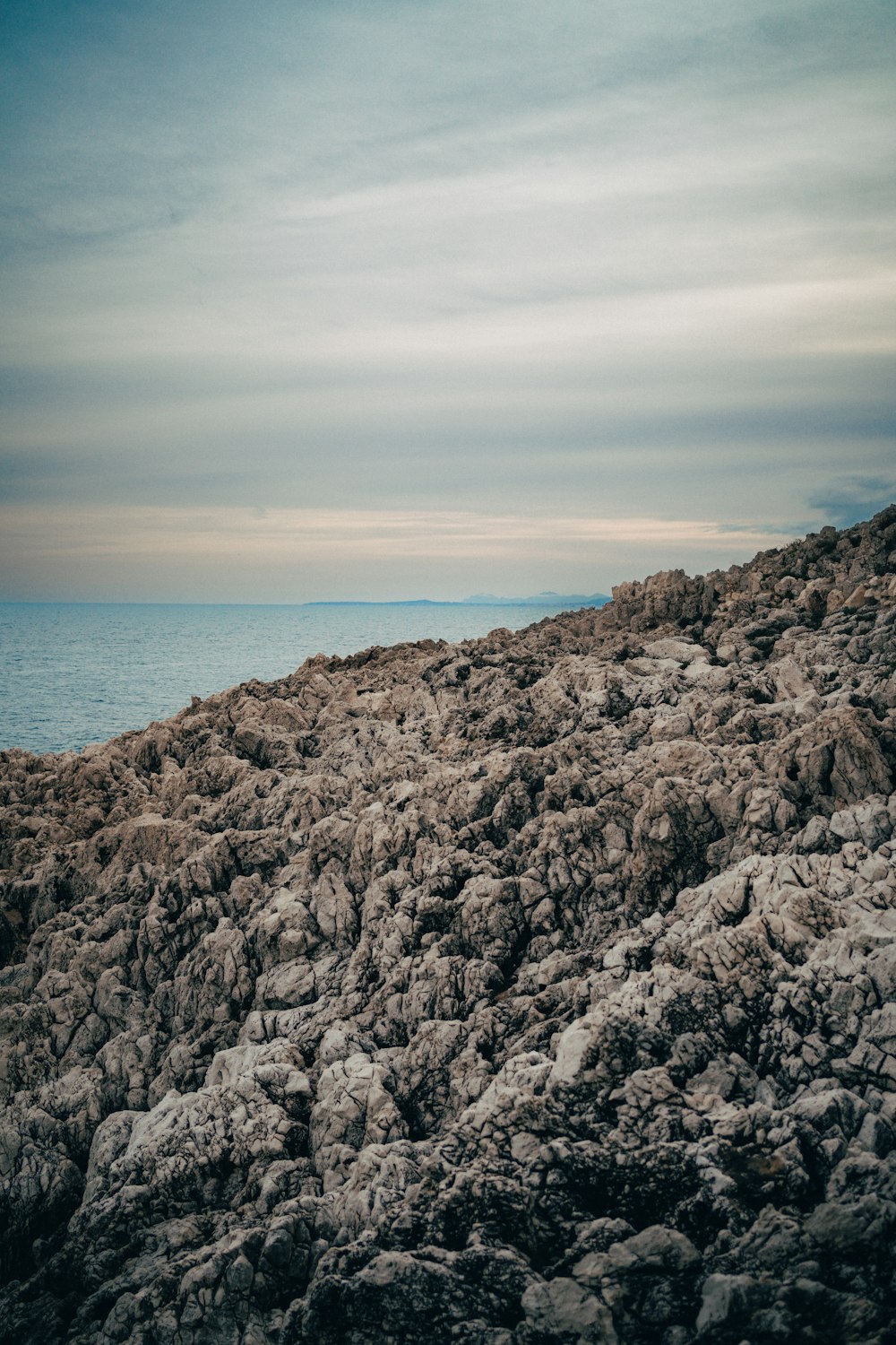 una persona parada en la cima de una colina rocosa junto al océano