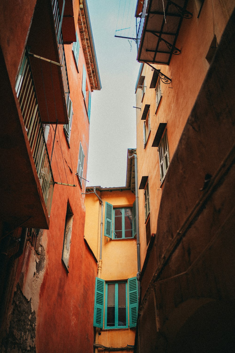 a narrow alleyway between two buildings with shutters open