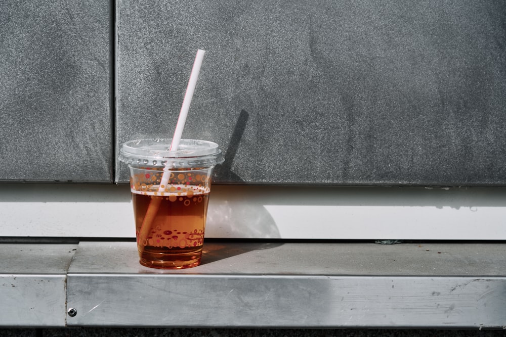 a cup with a straw in it sitting on a window sill