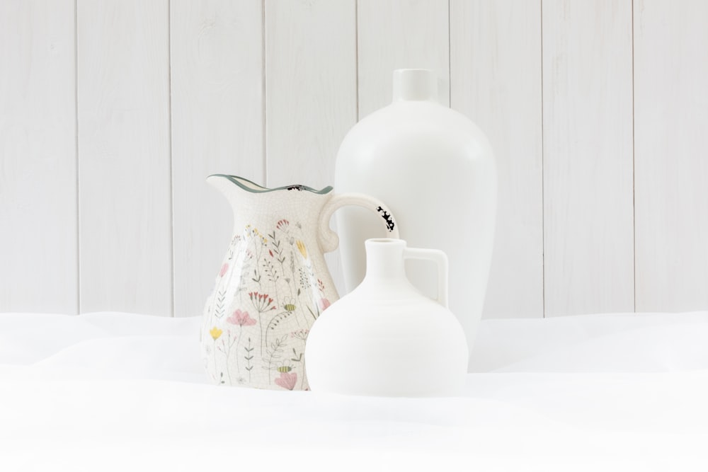 three white vases sitting next to each other on a white surface