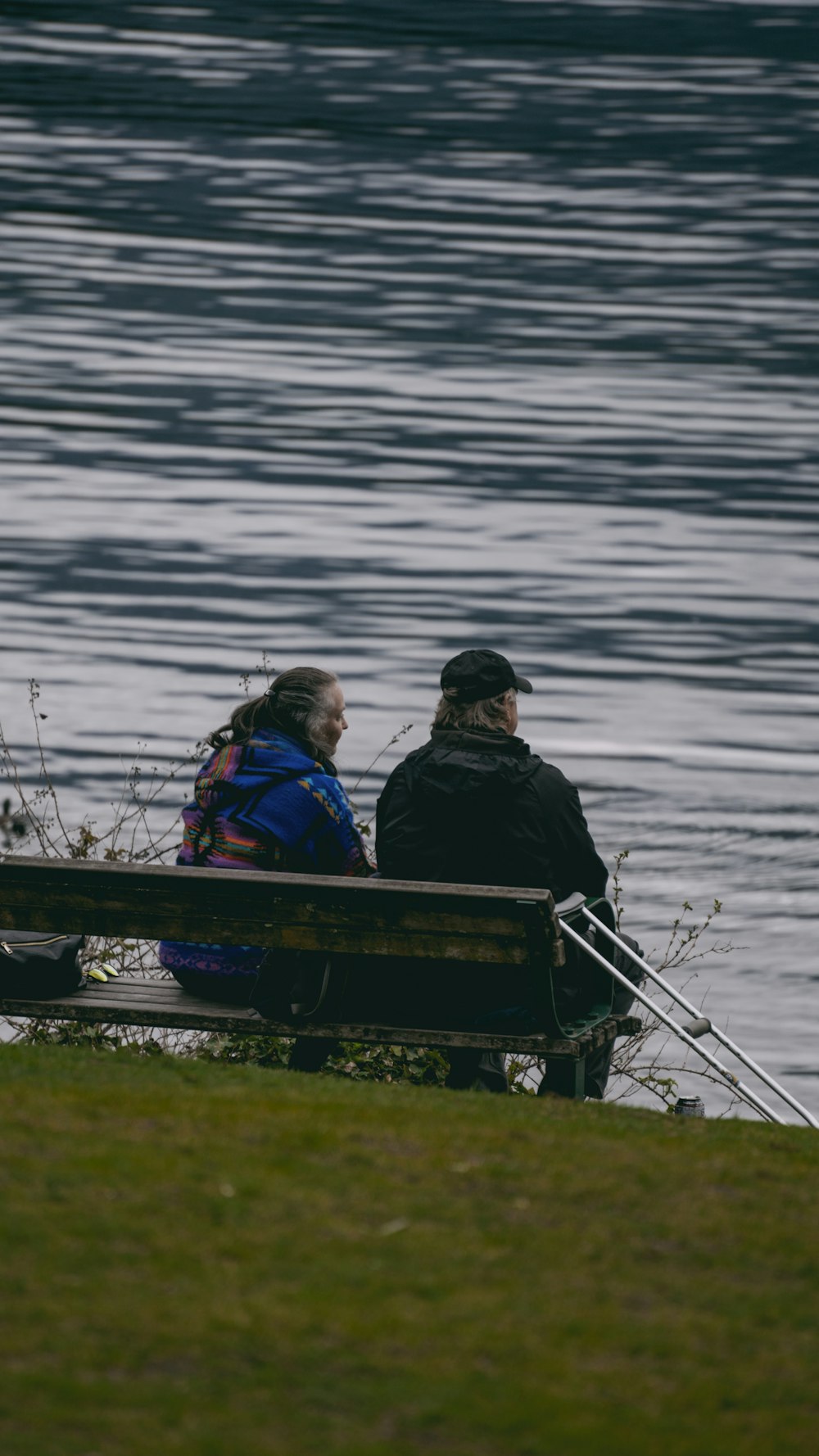 two people sitting on a bench near the water