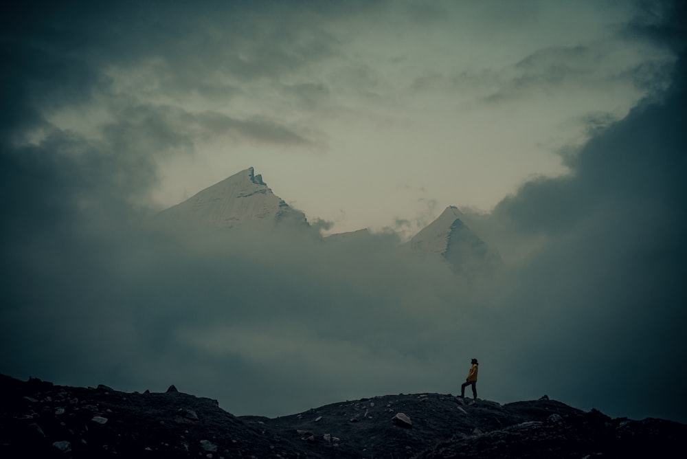 a man standing on top of a mountain under a cloudy sky