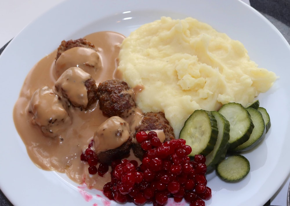 a white plate topped with meatballs, mashed potatoes and cucumbers