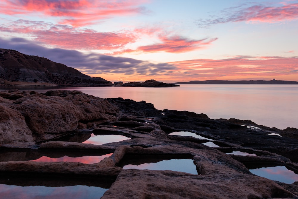 a rocky shore with a body of water at sunset