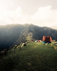 a tent set up on a grassy hill with mountains in the background