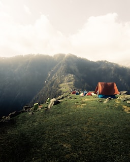 a tent set up on a grassy hill with mountains in the background