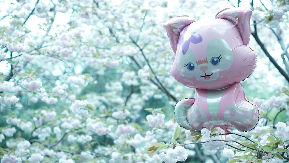 a pink cat balloon sitting on top of a tree filled with white flowers