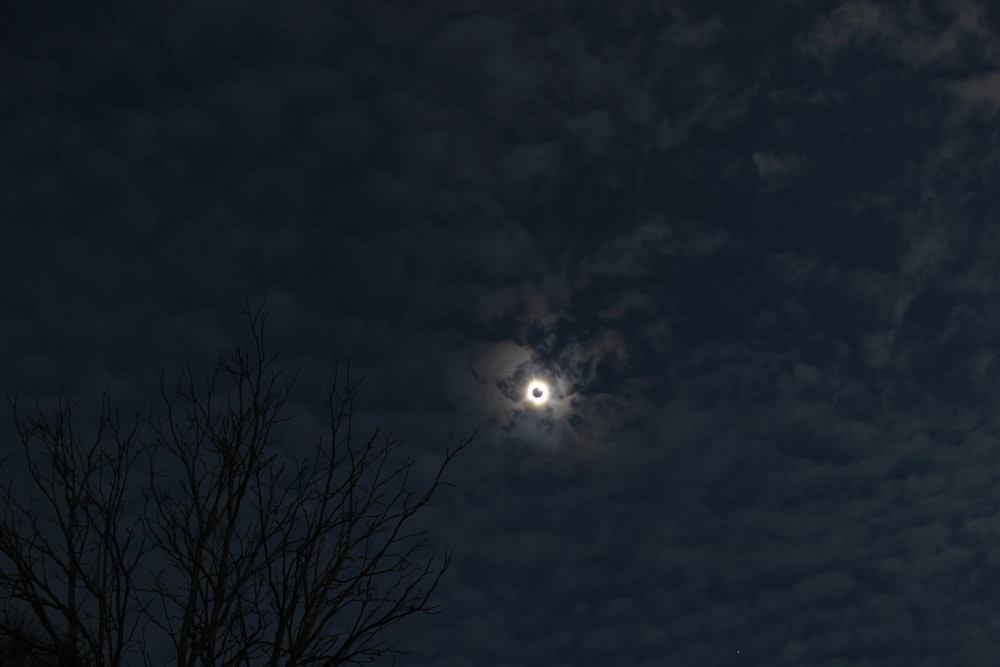 a full moon is seen through the clouds above a tree