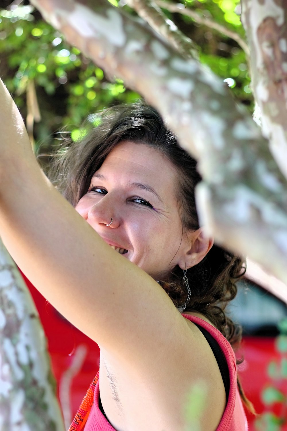 a woman in a pink shirt is reaching up to a tree