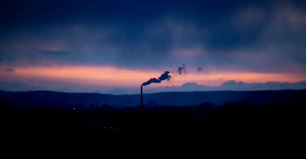 a smokestack emits from a pipe at dusk
