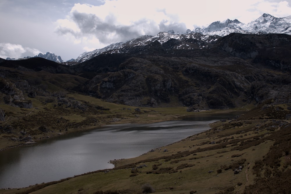 a lake surrounded by mountains under a cloudy sky