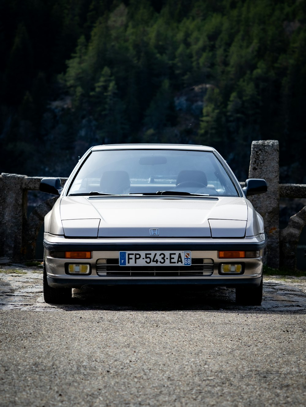 a white car parked in front of a stone fence